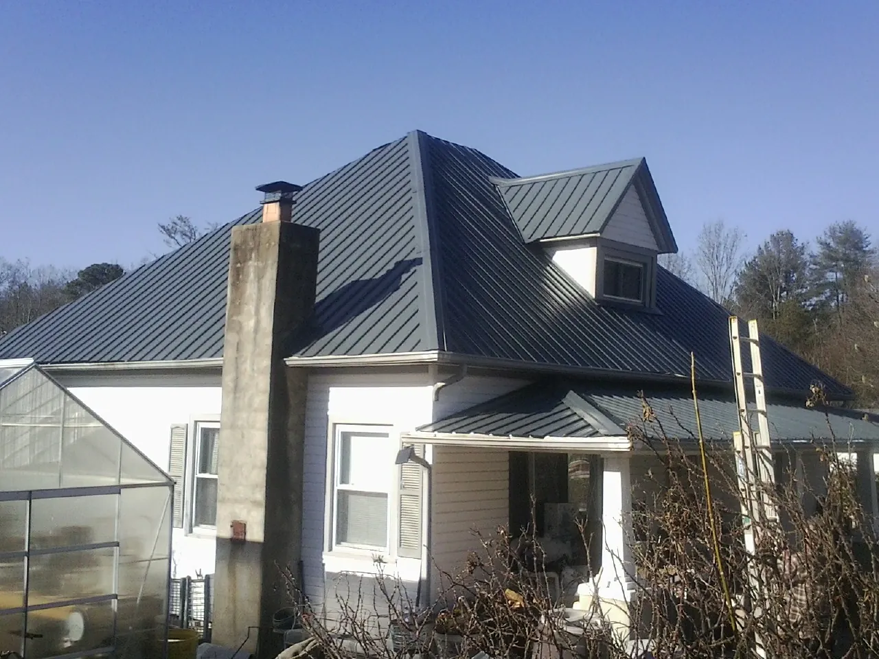 Dark blue standing seam metal roof on a white farmhouse with dormer — Slate & Tile Roof Repair by Roofing Brothers in Alvaton