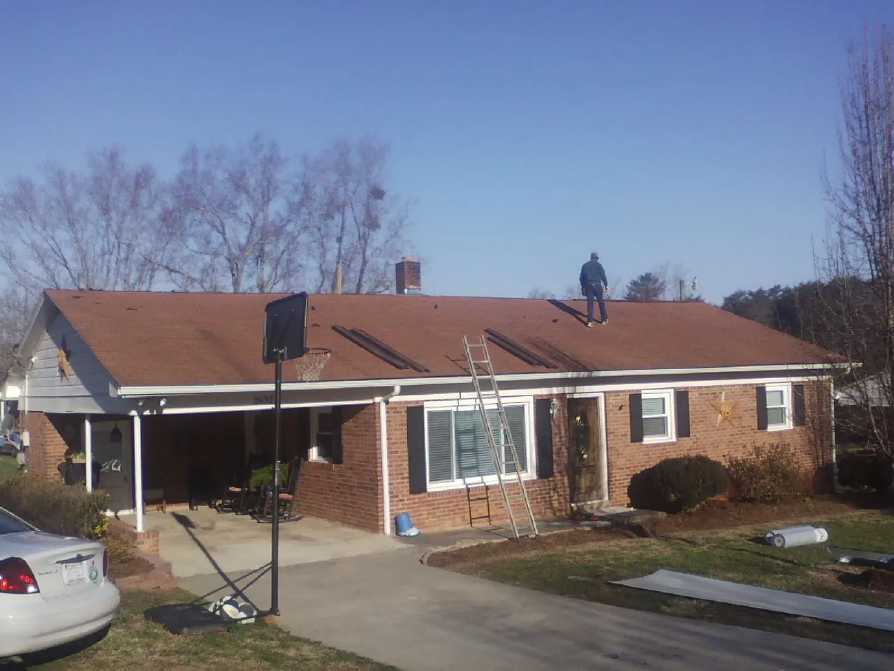 Roofer stripping a shingle roof on a brick ranch before metal panels in Alvaton