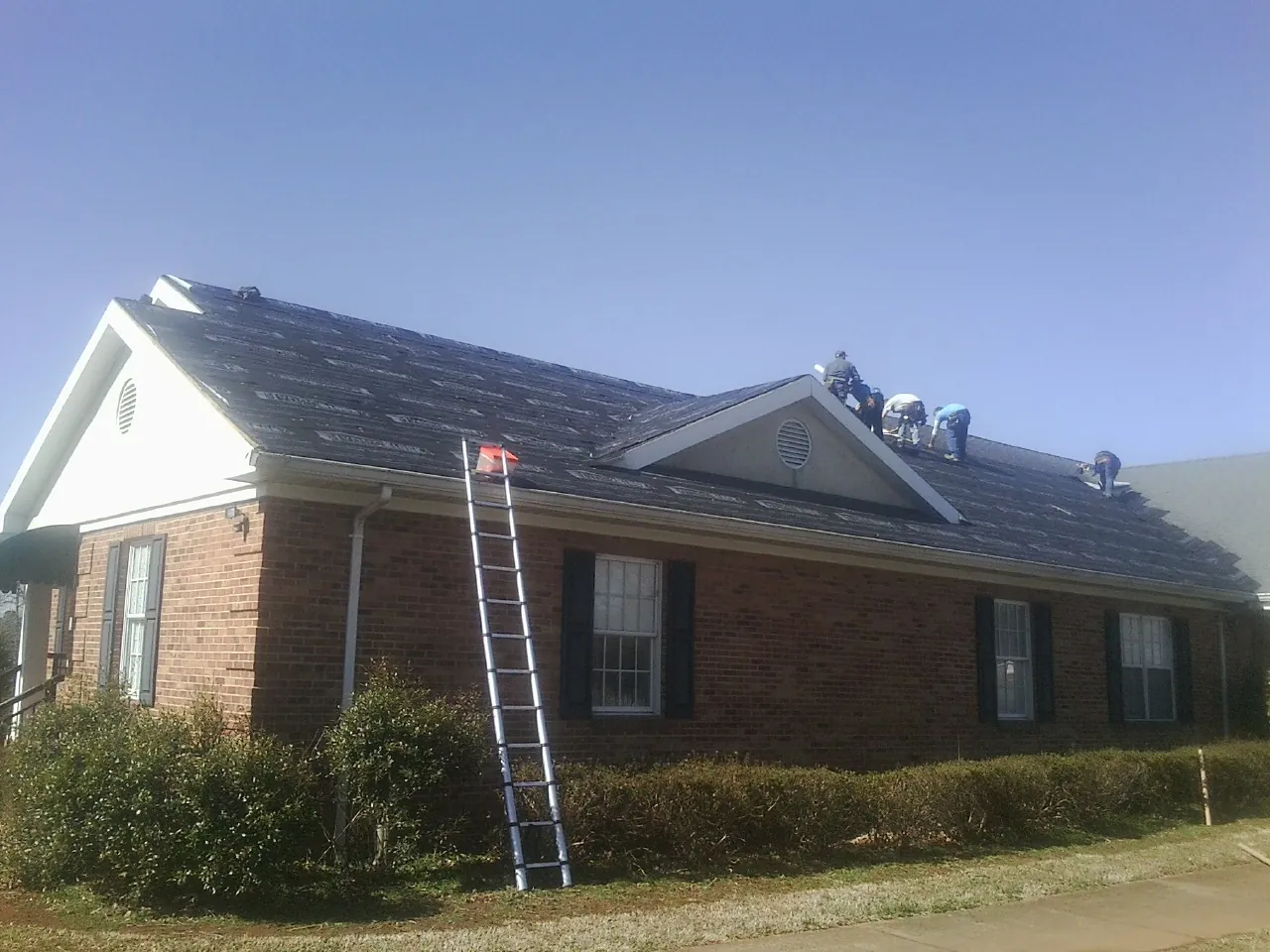 Crew tearing shingles off a brick ranch roof with a ladder set — Emergency Roof Repair work by our crew in Alvaton