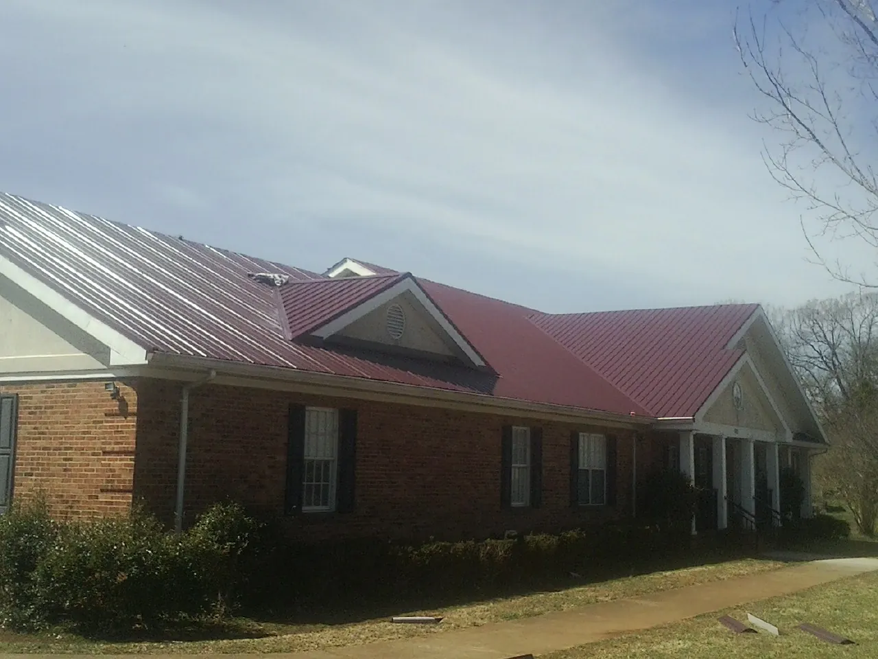 Red metal roof with gabled entries on a long brick building, from a Hail Damage Roof Repair job in Alvaton