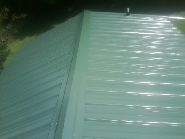 New green metal panels meeting at the ridge of a roof — Flat Roof Repair work by our crew in Alvaton
