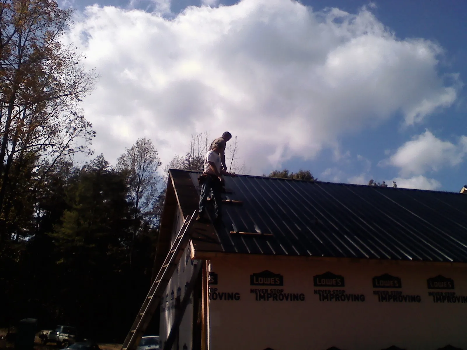Roofer fastening dark metal panels high against a cloudy sky, from a Roof Inspection job in Alvaton