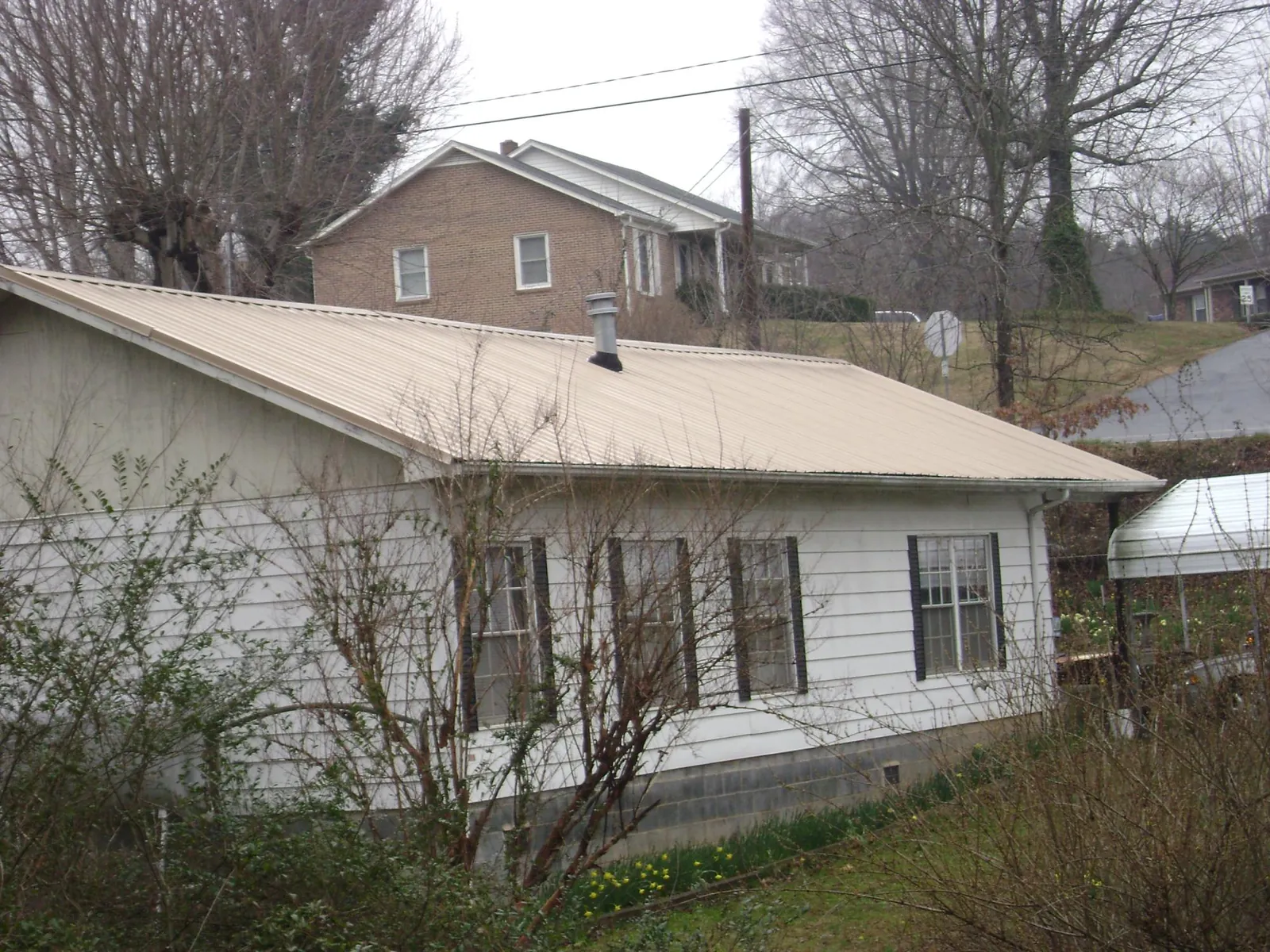 Tan metal roof on a white sided house set into a hillside — Commercial Roofing by Roofing Brothers in Alvaton