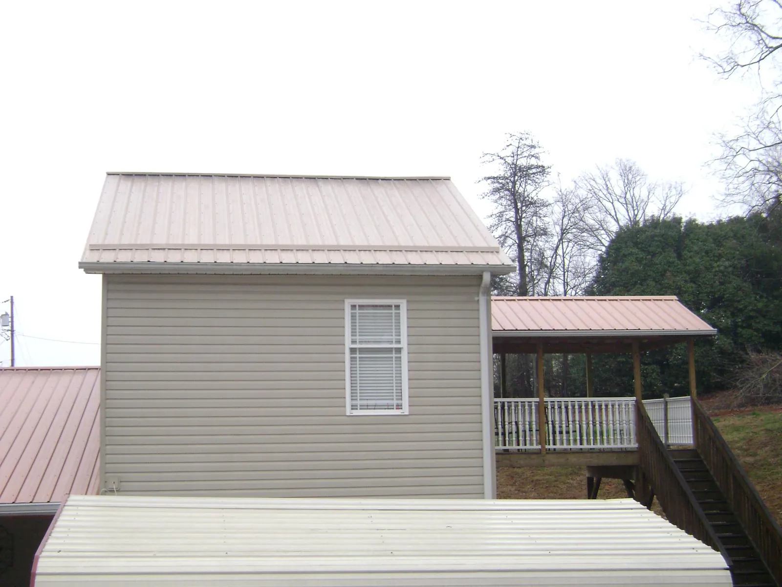 Tan metal roofs on a two story addition and attached porch, from a Roof Replacement job in Alvaton
